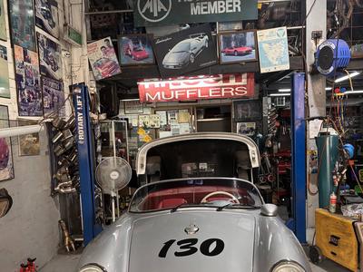 A silver Porsche 356 Speedster on the hoist beneath the MTA Authorised Member sign